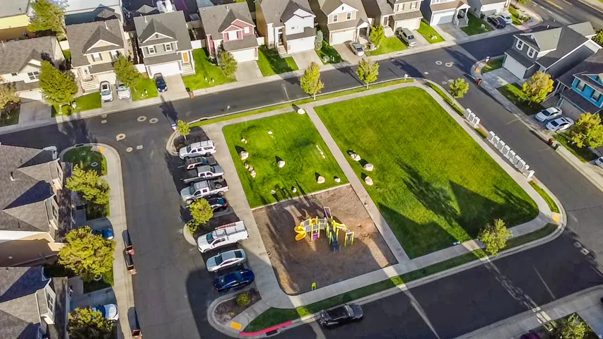 Neighborhood park with a playground, expansive green space, surrounding sidewalks, and mature trees