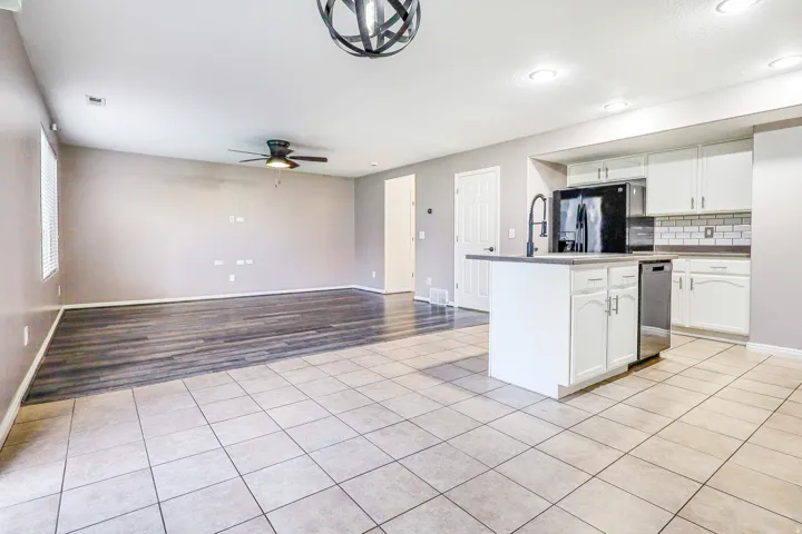 Open-concept kitchen and living area featuring a central island, white cabinetry, subway tile backsplash, and stainless steel appliances