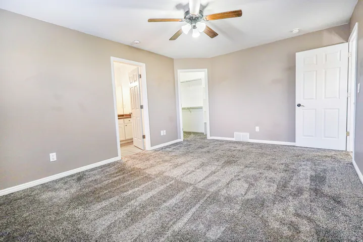 Plush carpeted flooring, neutral wall tones, ceiling fan with integrated lighting, two-panel interior doors, and a walk-in closet with built-in shelving