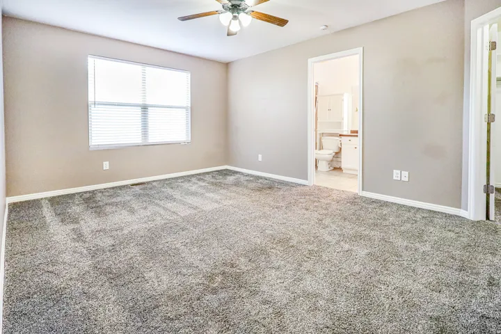 Carpeted interior with light-toned walls, ceiling fan, and window with blinds