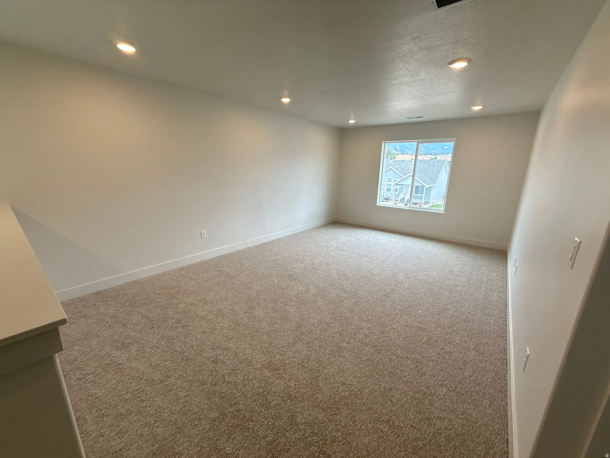 Plush carpeting, recessed lighting, and a window with white trim