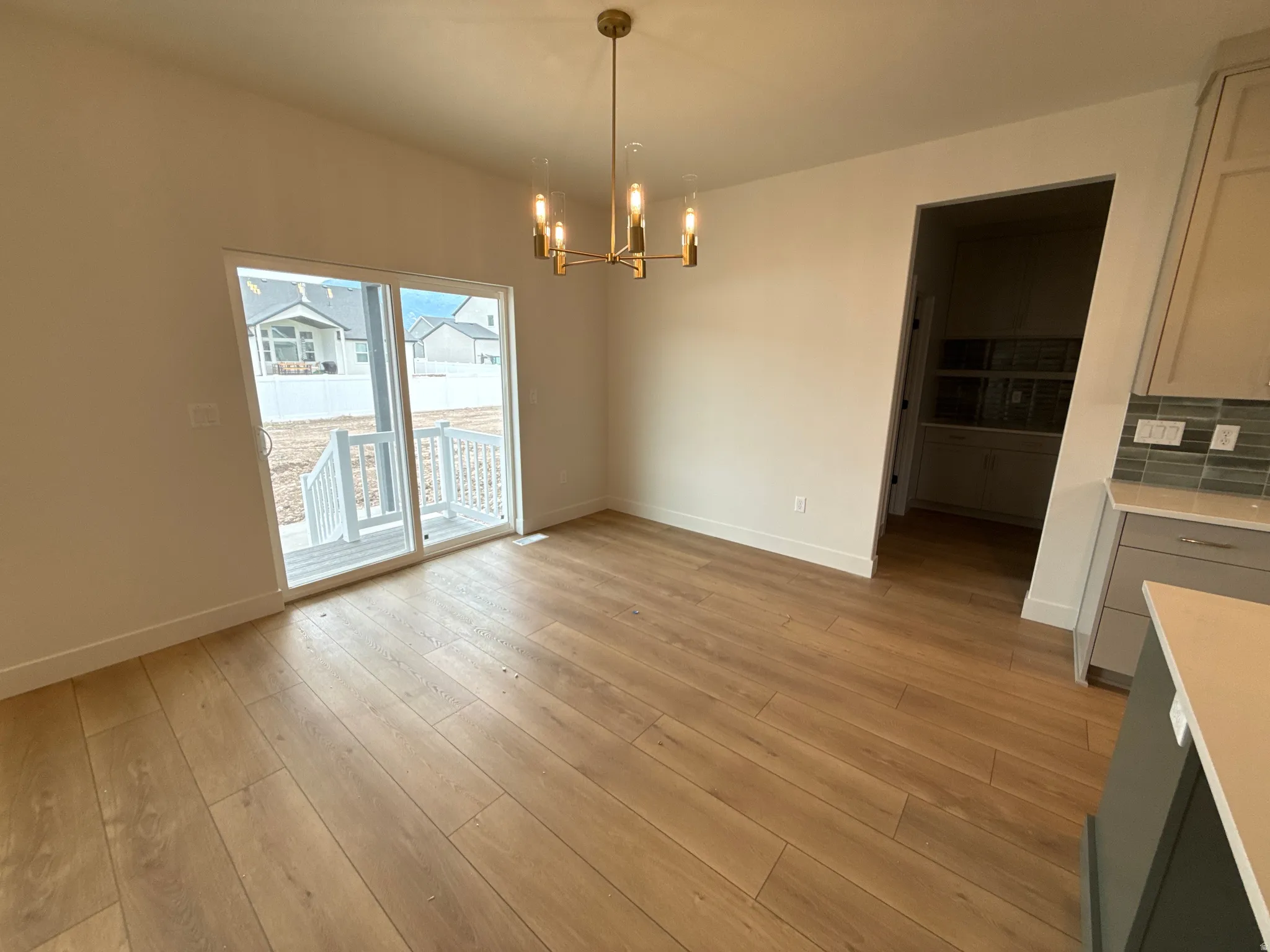 Wood-finish flooring, contemporary chandelier, sliding glass door, white porch railing, and light-toned wall paint