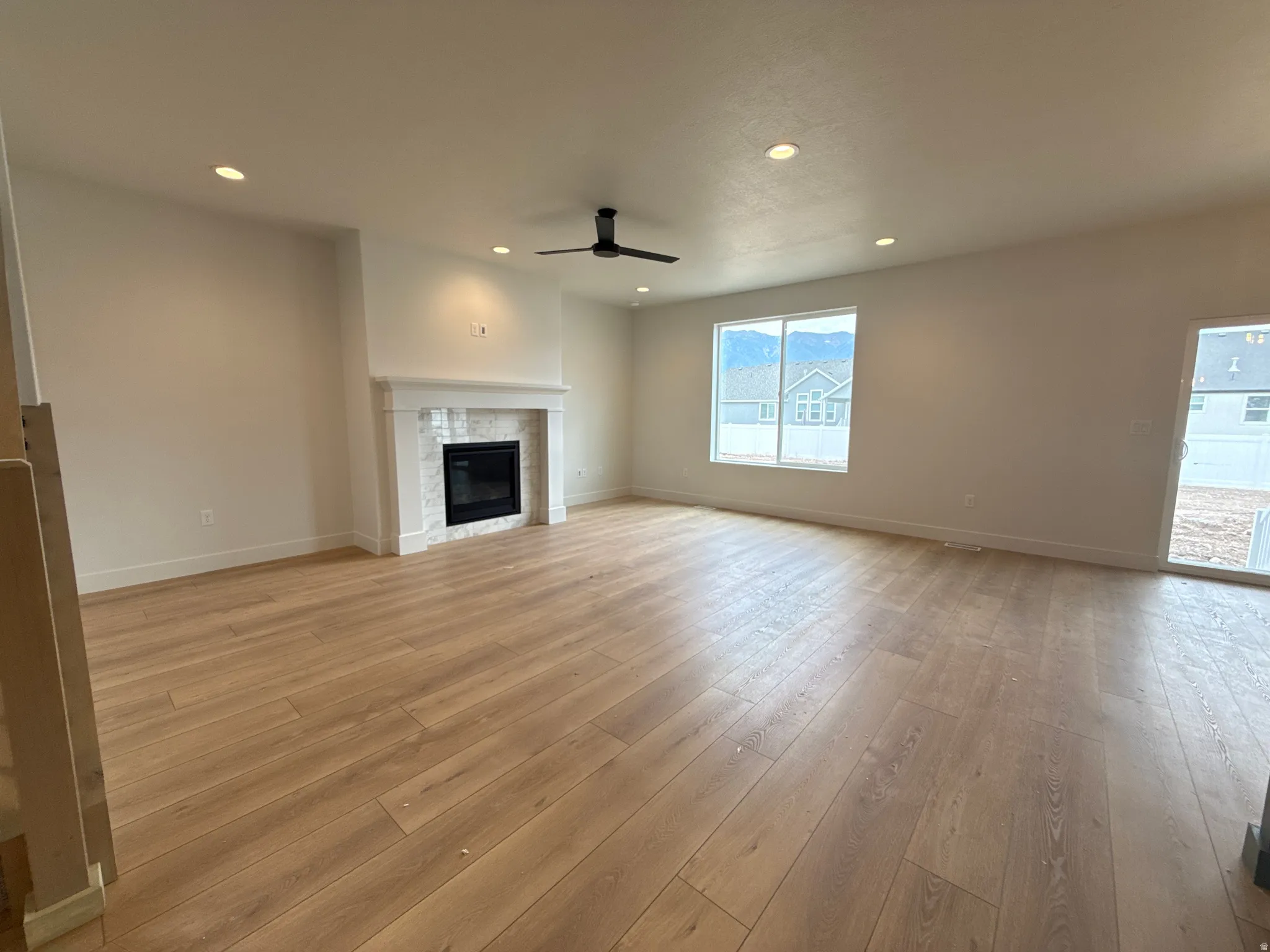 Spacious room featuring wood-finish flooring, a contemporary fireplace with a white mantel, recessed lighting, a ceiling fan, and large windows