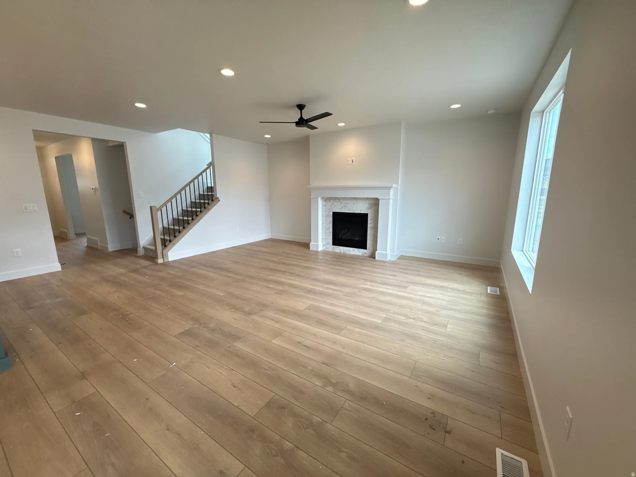 Wood-finish flooring, recessed ceiling lighting, a fireplace with a decorative mantel and tile surround, and a ceiling fan with integrated lighting