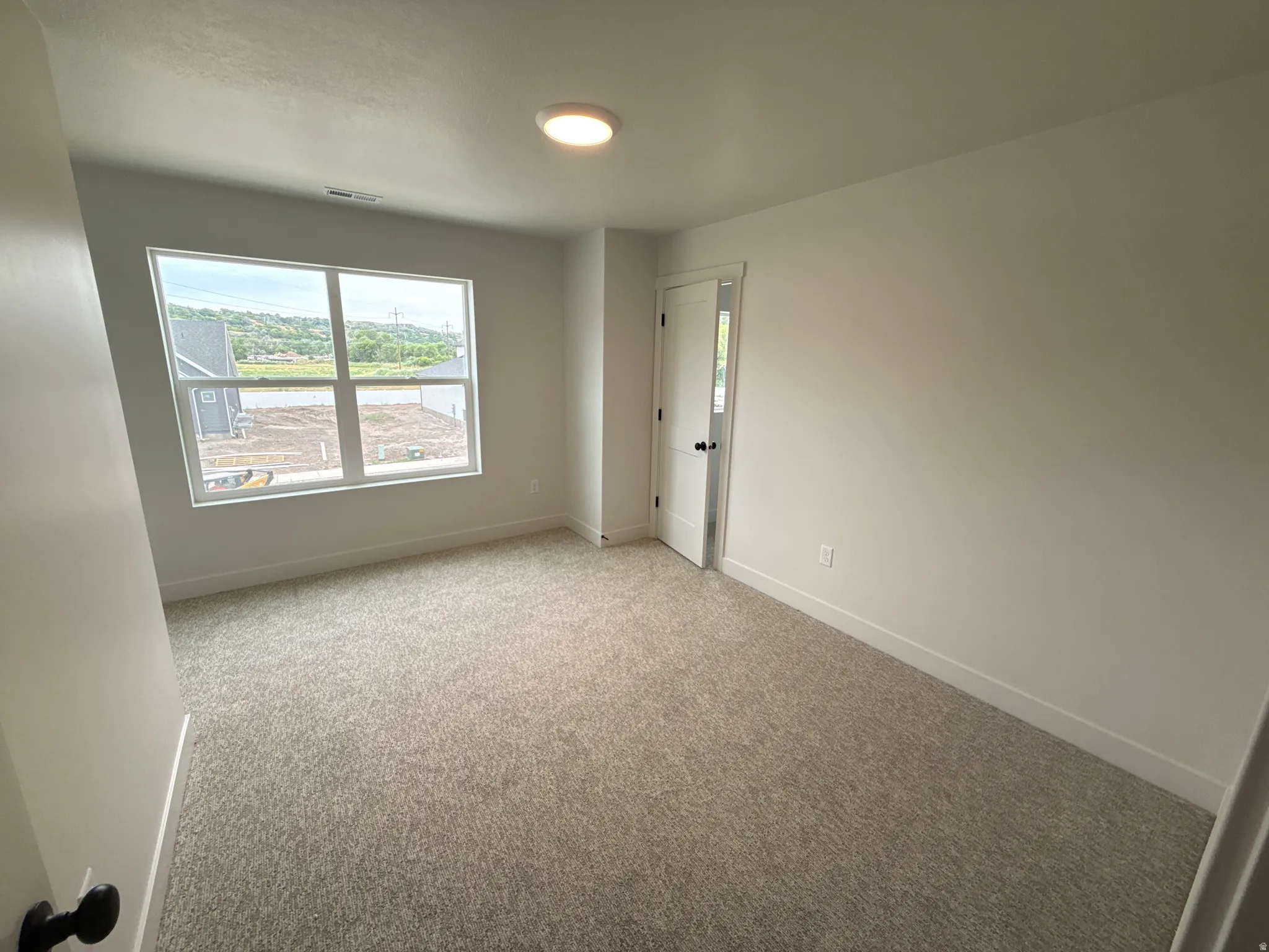 Neutral-toned carpeting, ample natural light, recessed ceiling fixture, white interior door with matte black hardware, and crisp white walls
