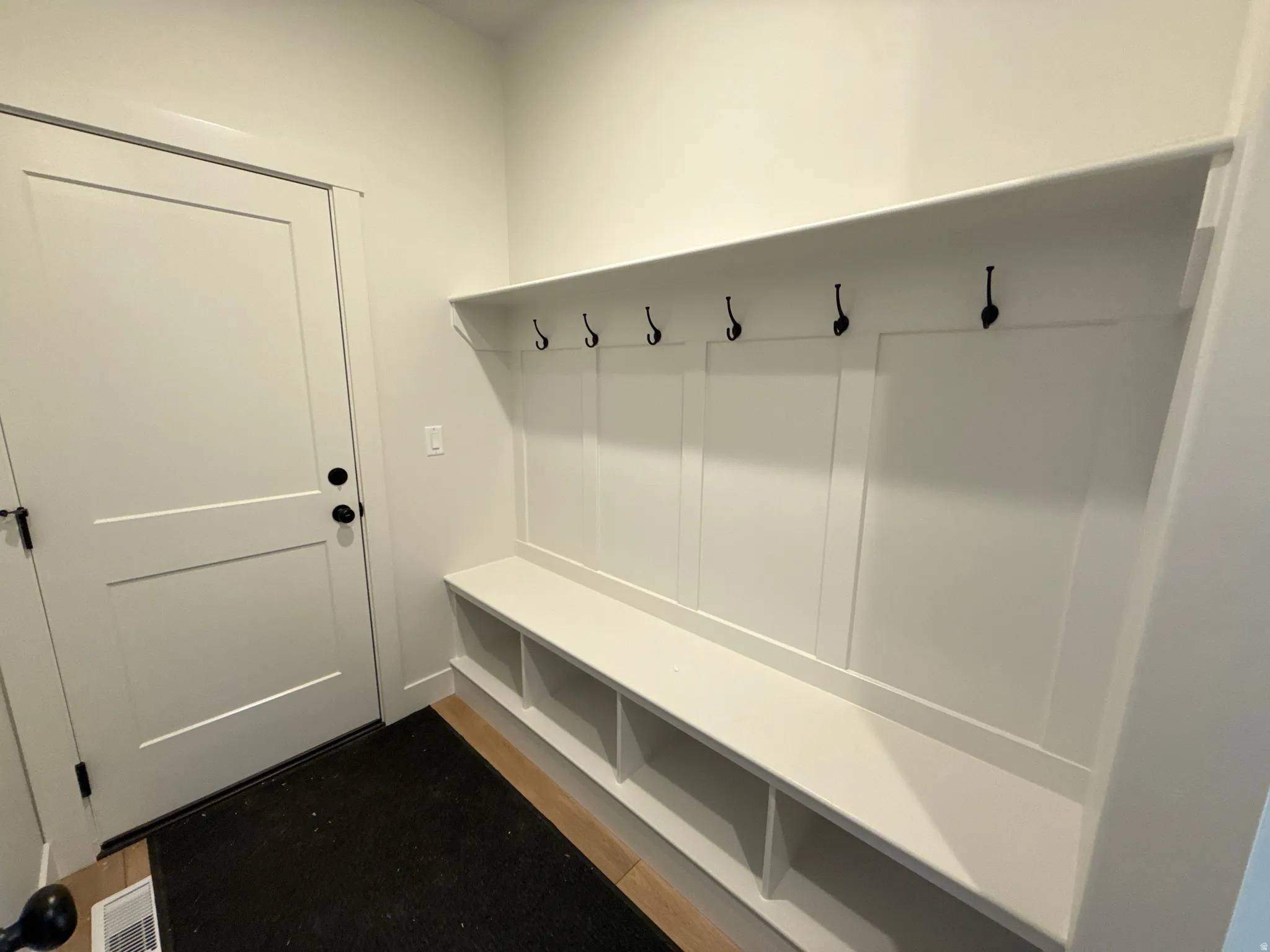 Mudroom featuring white built-in storage with cubbies, built-in bench, and black coat hooks