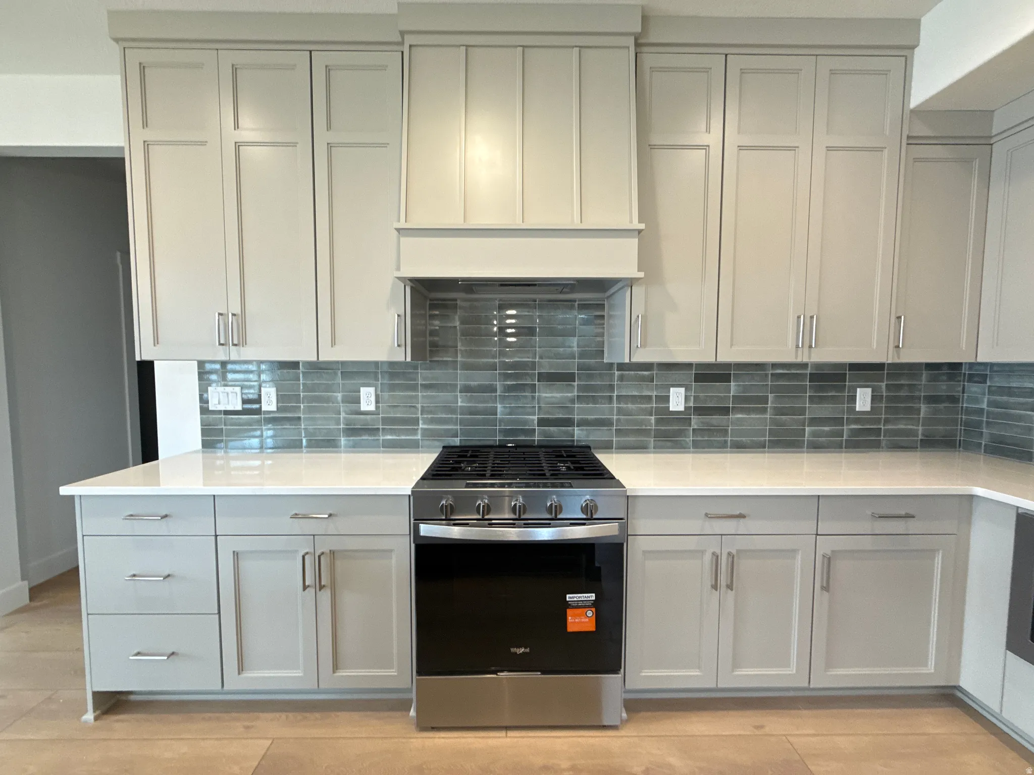 Kitchen featuring light gray cabinetry, a range with a stainless steel finish, white countertops, a tile backsplash, and wood-finish flooring