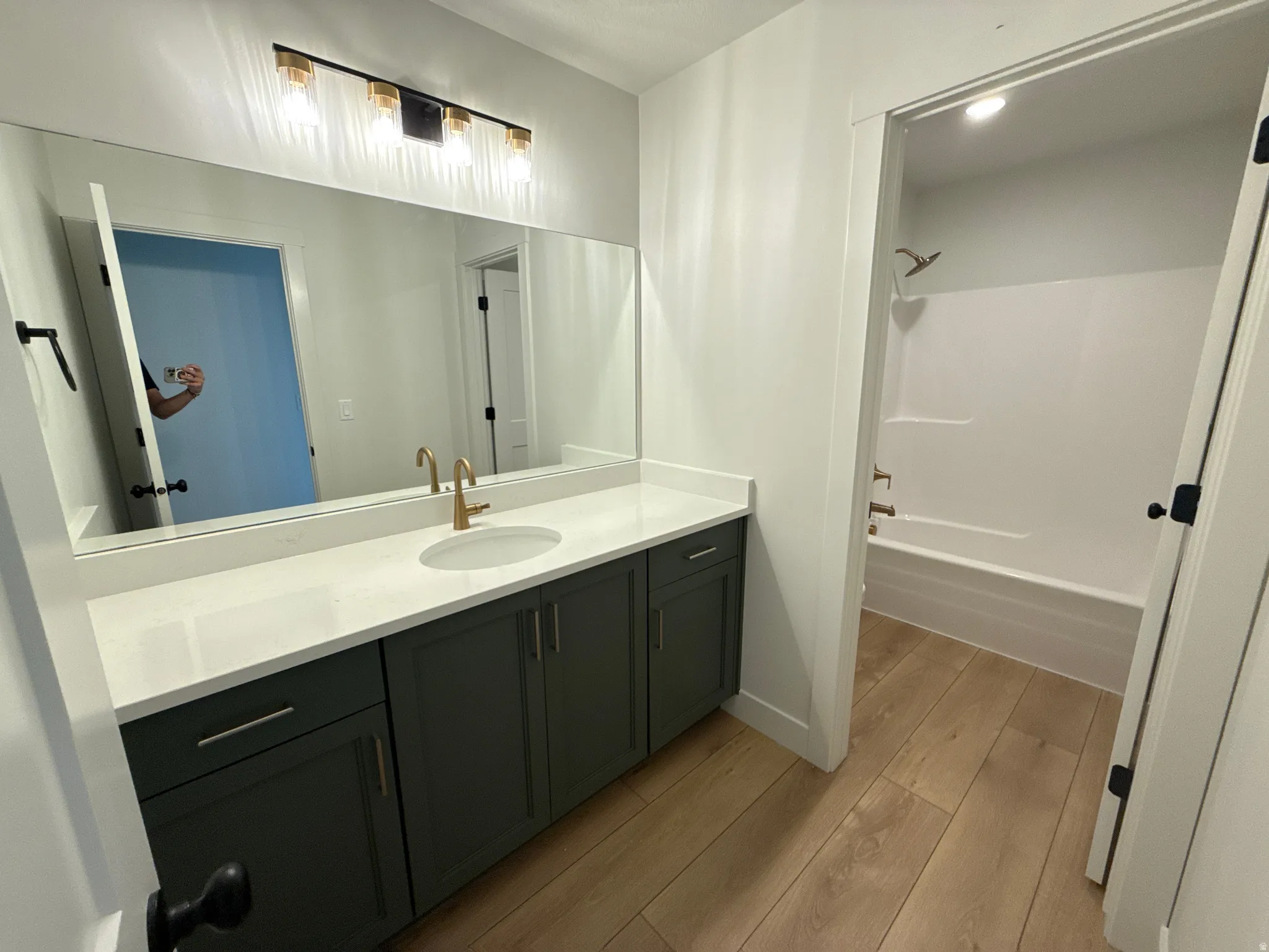 Vanity with a white countertop and brass-finish faucet, wood-finish flooring, and a shower-tub combination