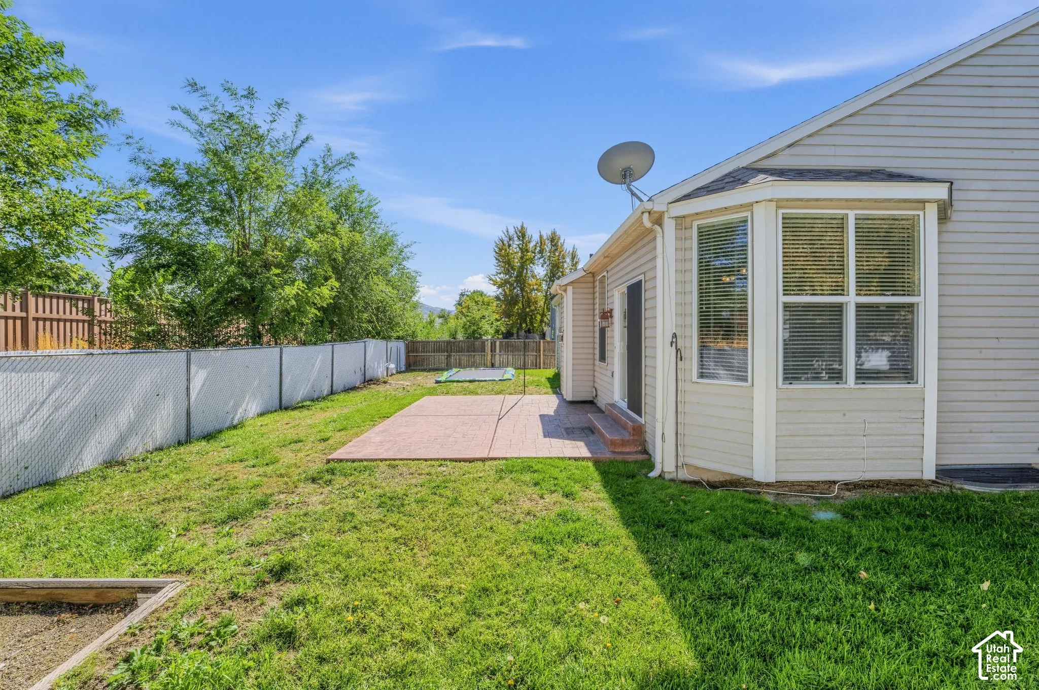 Expansive rear yard with a concrete patio, bay windows, and a sliding glass door