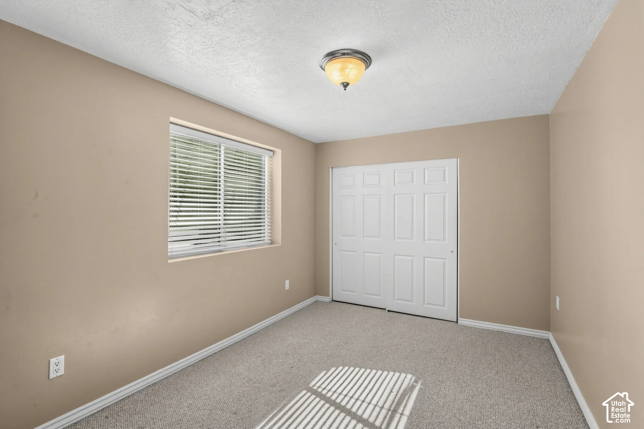 Recessed window with blinds, bi-fold closet doors, wall-mounted ceiling light fixture, and neutral-toned carpeting