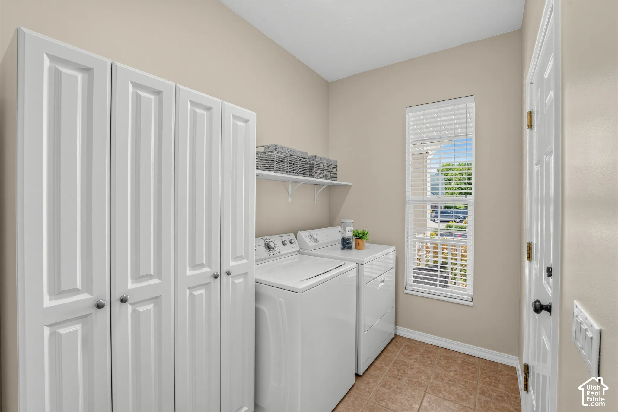 Laundry area featuring white built-in cabinetry, ceramic tile flooring, and a single window with blinds