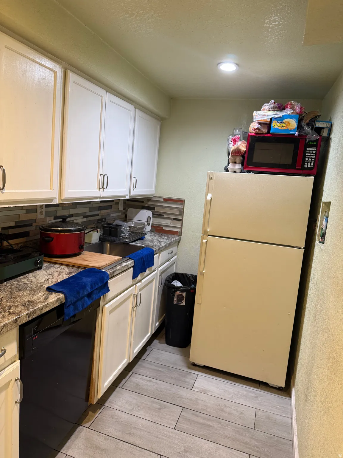 White cabinetry, patterned backsplash, light-toned flooring, integrated dishwasher, and recessed lighting