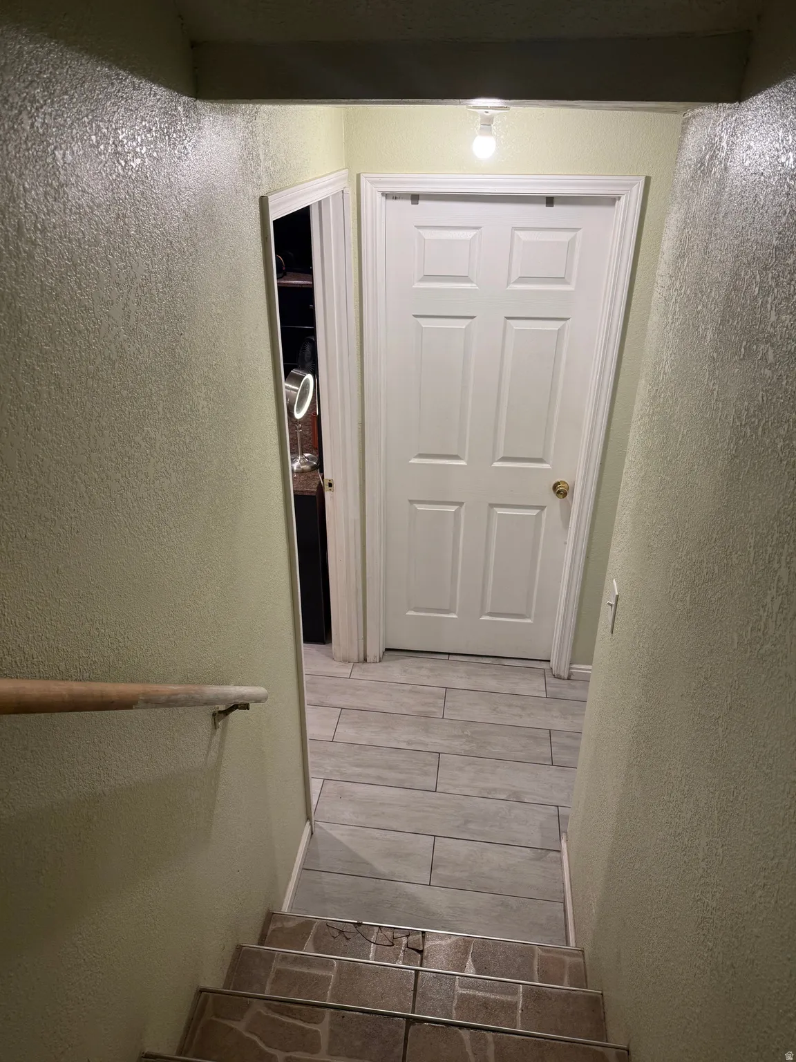 Staircase with a wood handrail leading to a landing with wood-finish tile flooring