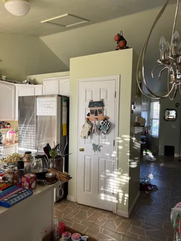 White paneled cabinetry, stainless steel refrigerator, white paneled door, and tile flooring