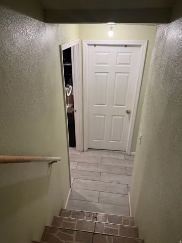 Staircase with a wood handrail leading to a landing with wood-finish tile flooring