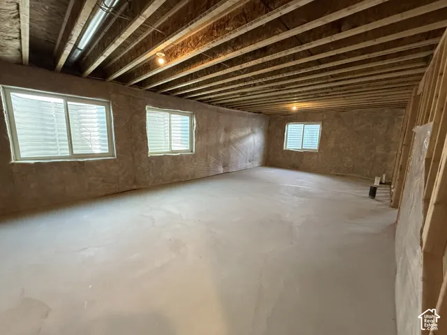 Unfinished space featuring exposed timber joist ceiling, concrete flooring, three sliding windows with window wells, and insulated wall paneling