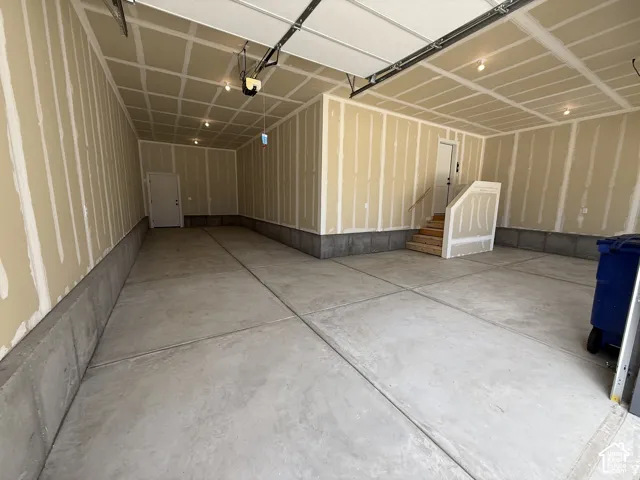Spacious multi-car garage featuring finished concrete flooring, drywall construction, recessed lighting, and a dedicated staircase with a railing