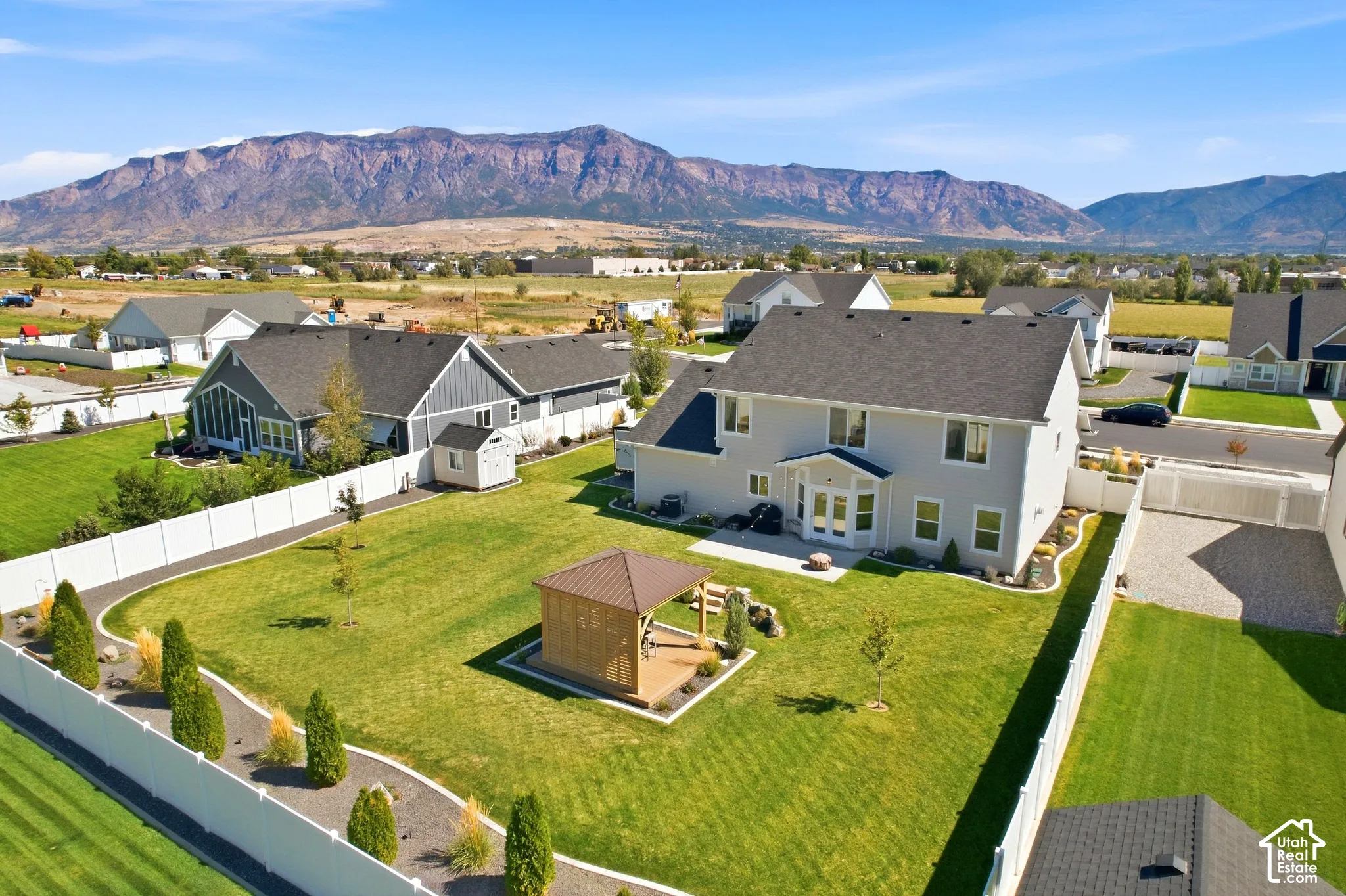 Expansive backyard featuring a large lawn, white privacy fencing, and a built-in gazebo
