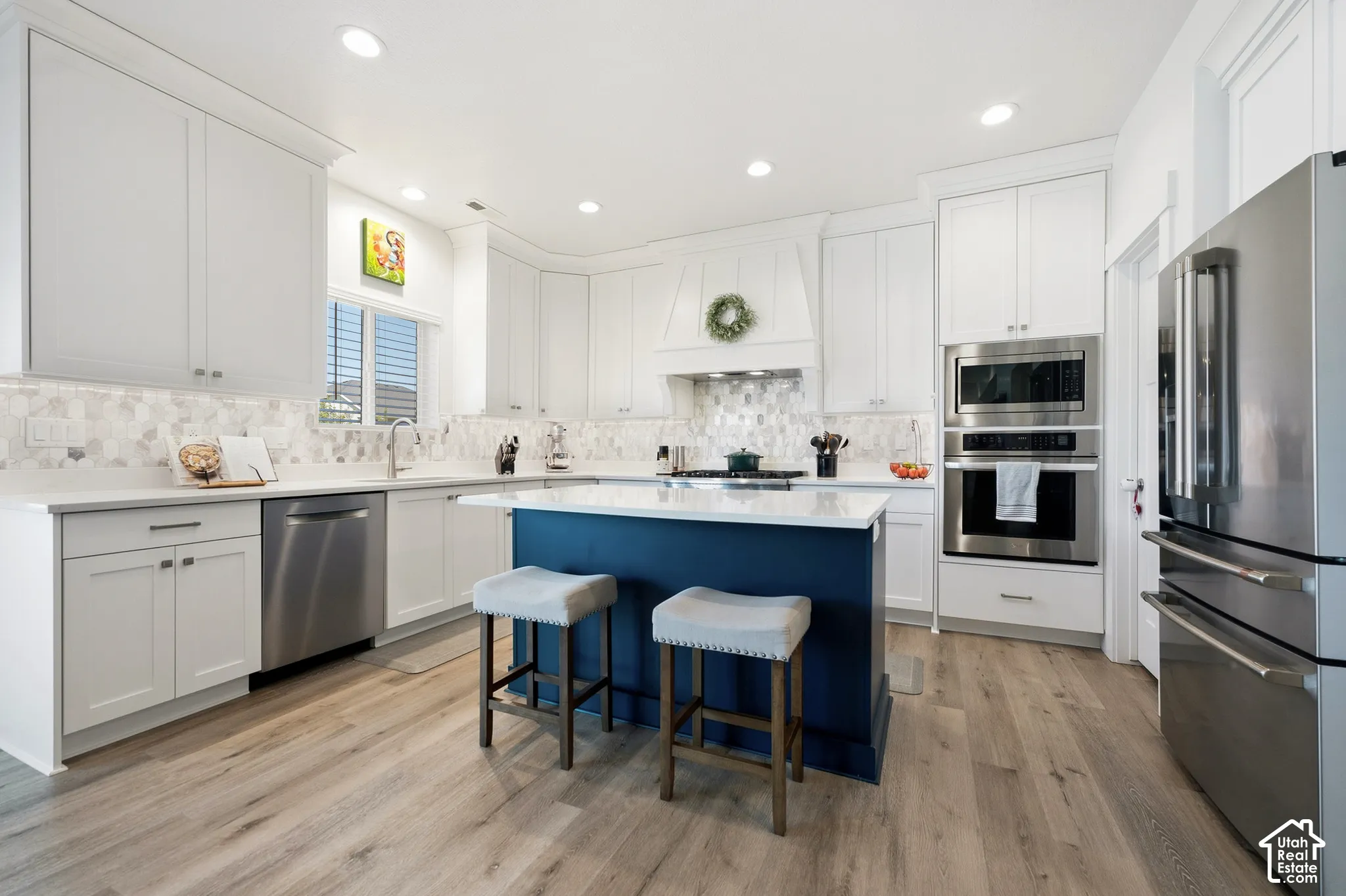 Kitchen featuring white cabinetry, wood-finish flooring, stainless steel appliances, a center island with a countertop, and a tile backsplash