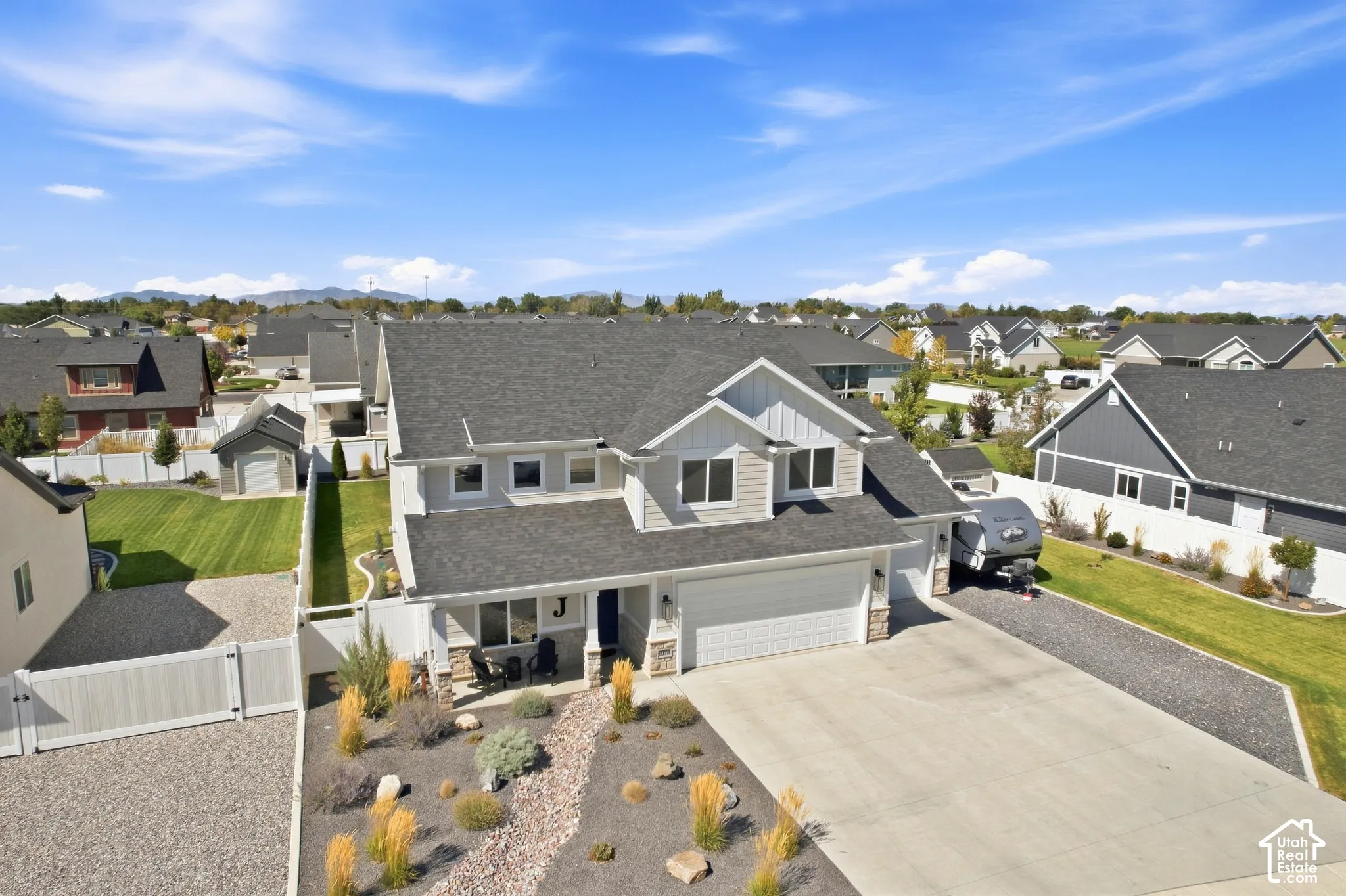 Contemporary exterior with light gray siding and stone accents, featuring a two-car garage, covered porch, and a gravel driveway with additional parking
