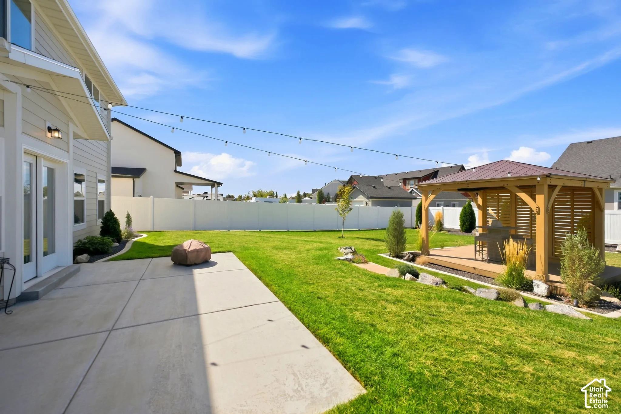 Expansive backyard featuring a manicured lawn, a concrete patio, and a covered wooden gazebo with a metal roof