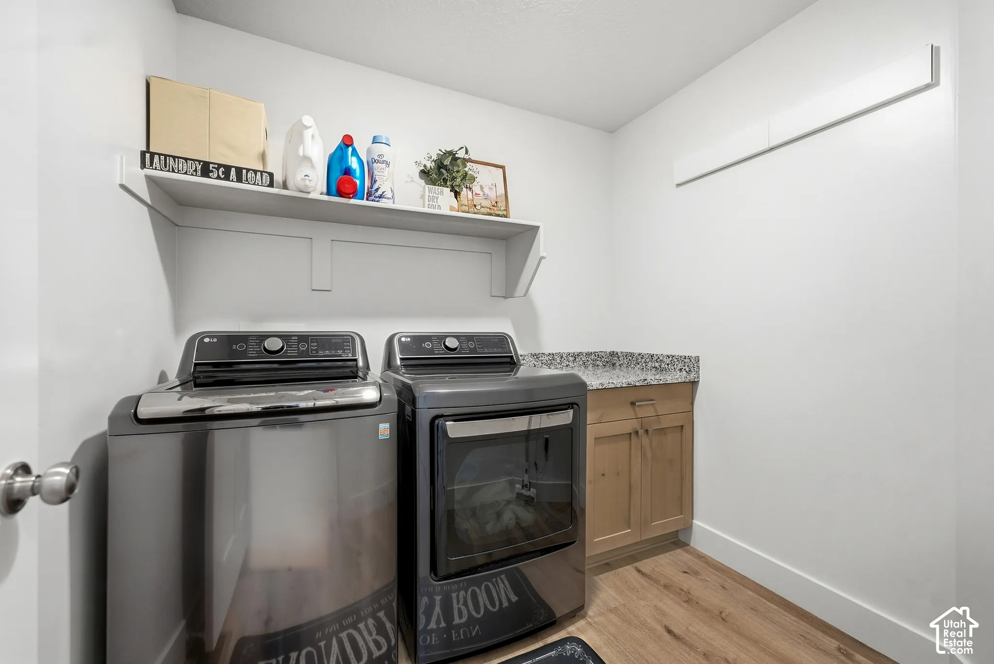 Laundry area featuring wood-finish flooring, built-in shelving, a stone-finish countertop, and light wood cabinetry