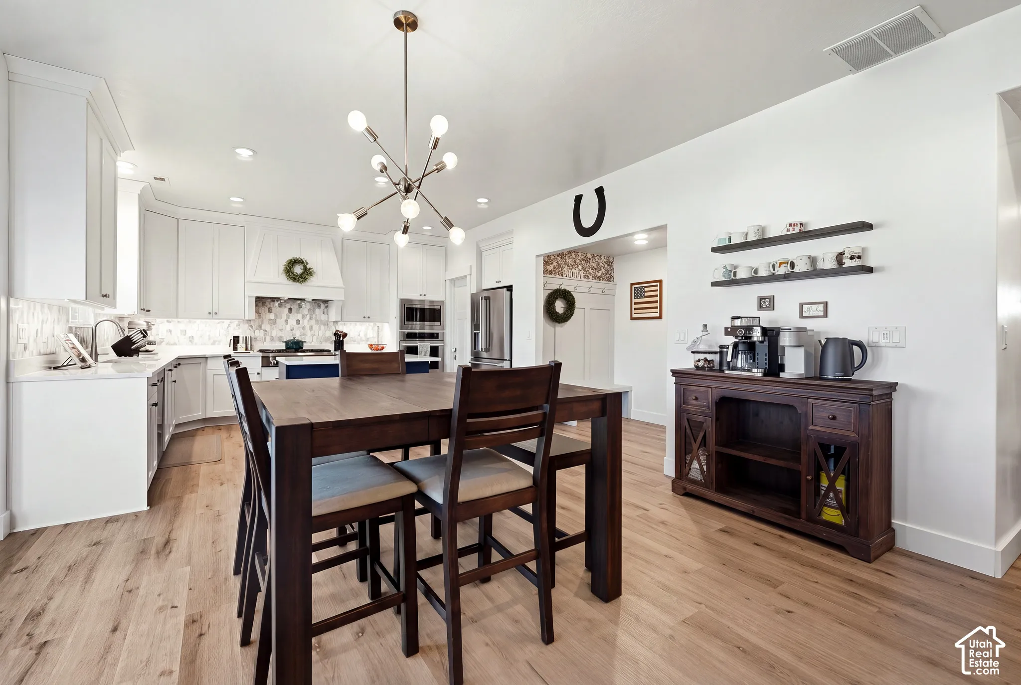 Gourmet kitchen with white cabinetry, tile backsplash, stainless steel appliances, and a central dining counter