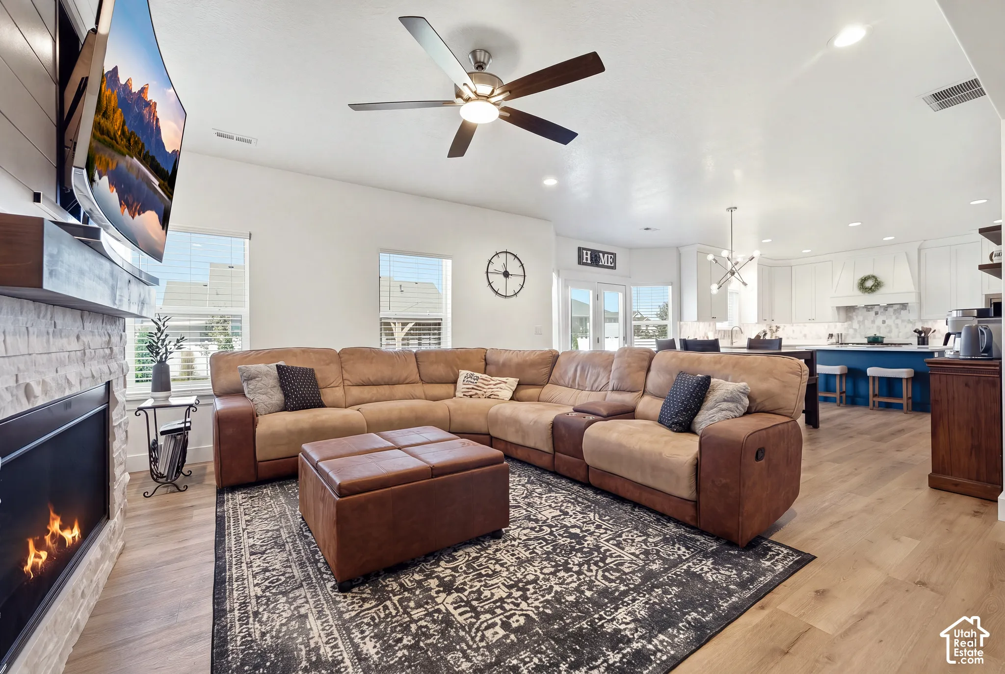 Open-concept living space with wood-finish flooring, a stone-clad fireplace, and a ceiling fan