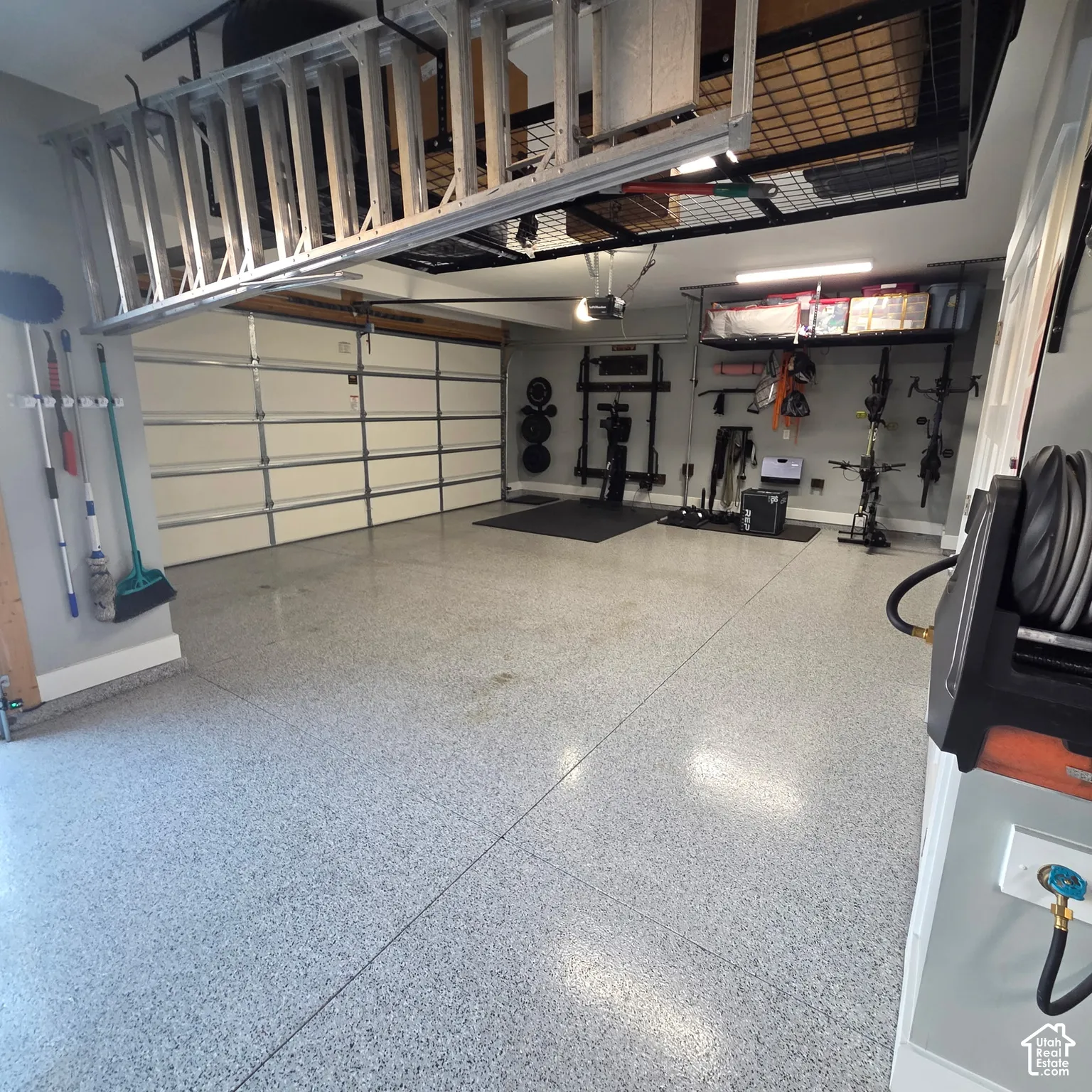 Spacious garage with light-colored epoxy flooring, overhead storage racks, integrated overhead lighting, and built-in wall organization systems