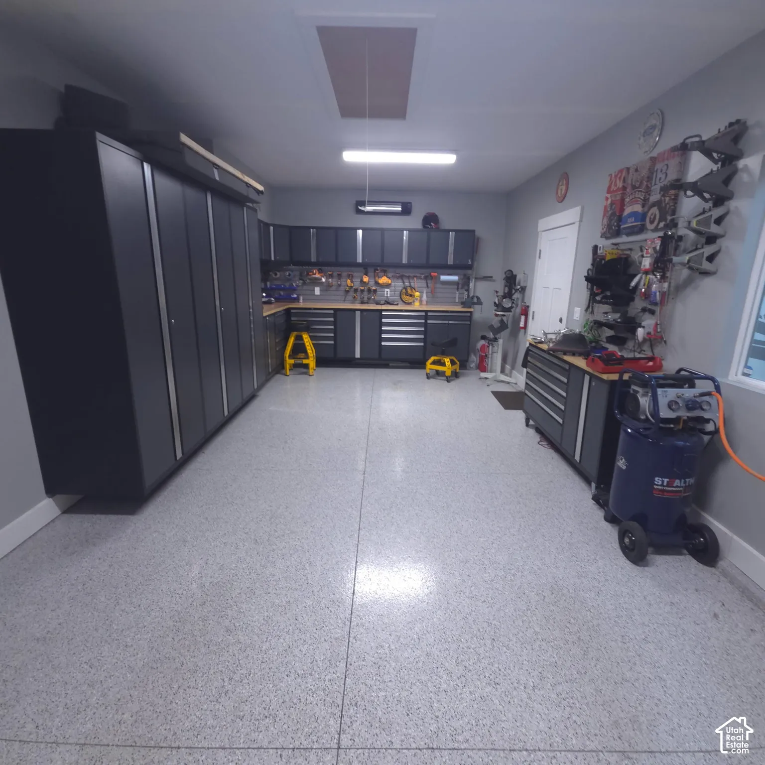 Epoxy garage flooring, extensive built-in cabinetry, integrated workbench, overhead lighting, and wall-mounted storage