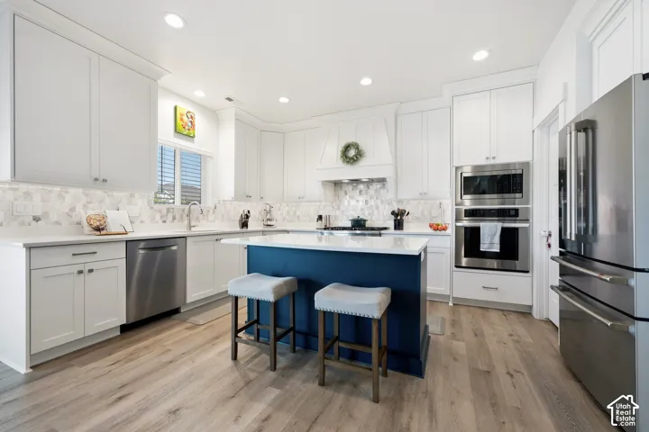 Kitchen featuring white cabinetry, wood-finish flooring, stainless steel appliances, a center island with a countertop, and a tile backsplash