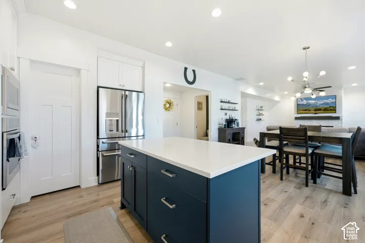 Bright kitchen featuring a central island with white countertop, stainless steel appliances, recessed lighting, and wood-finish flooring