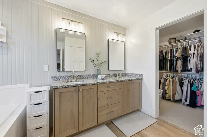 Dual vanity with granite countertops, light wood-finish cabinetry, and vertical plank wall paneling