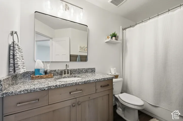 Bathroom featuring a single vanity with stone countertops, wood-finish cabinetry, and a framed mirror