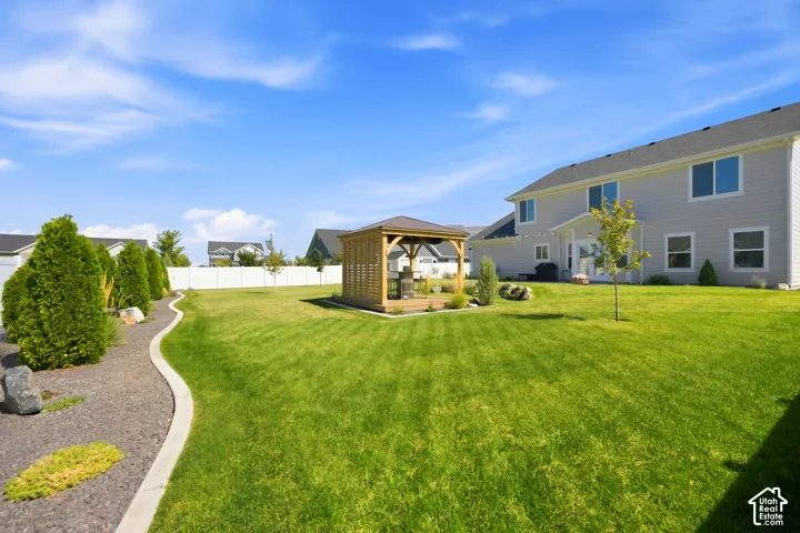 Expansive backyard featuring a manicured lawn, established landscaping, privacy fencing, and a built-in gazebo