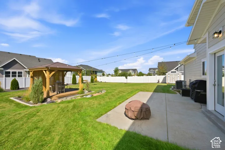 Expansive backyard featuring a manicured lawn, concrete patio, built-in wooden gazebo, and white privacy fencing