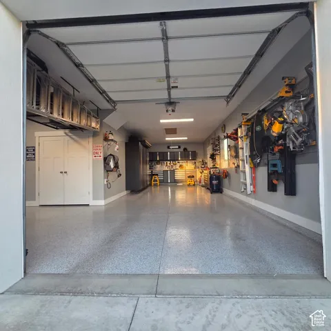 Attached garage featuring an epoxy floor, extensive wall-mounted storage, built-in cabinetry, overhead lighting, and an overhead storage rack