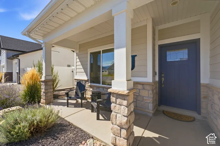 Covered front porch featuring stone-clad columns, durable siding, a large picture window, and a paneled entry door with decorative glass