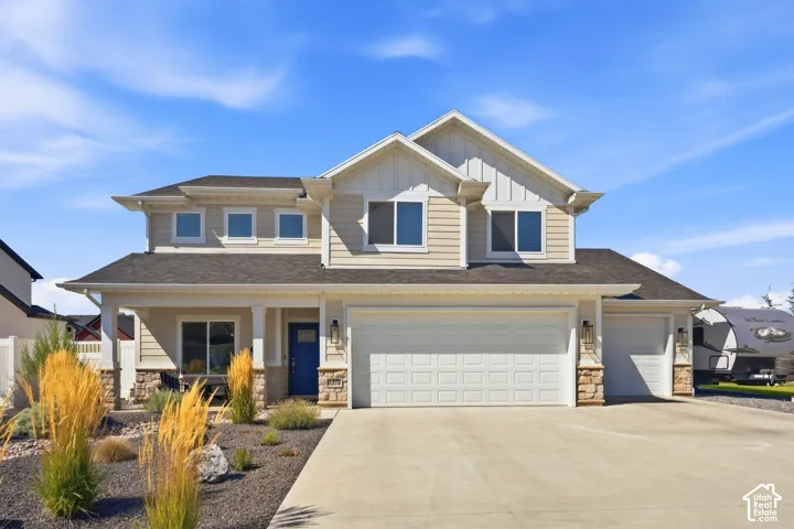 Two-story residence featuring light-toned siding, a multi-car garage, and a covered porch