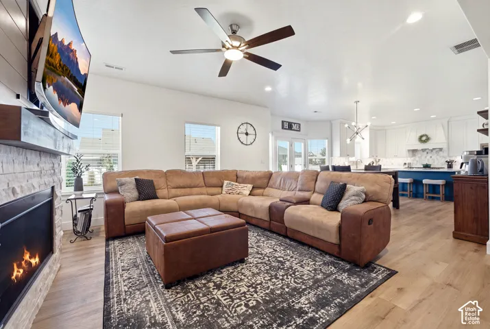 Open-concept living space with wood-finish flooring, a stone-clad fireplace, and a ceiling fan