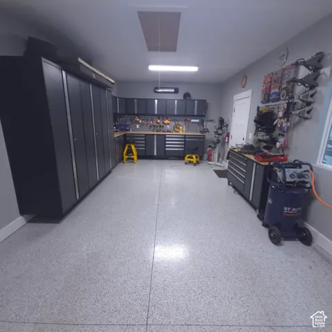 Epoxy garage flooring, extensive built-in cabinetry, integrated workbench, overhead lighting, and wall-mounted storage