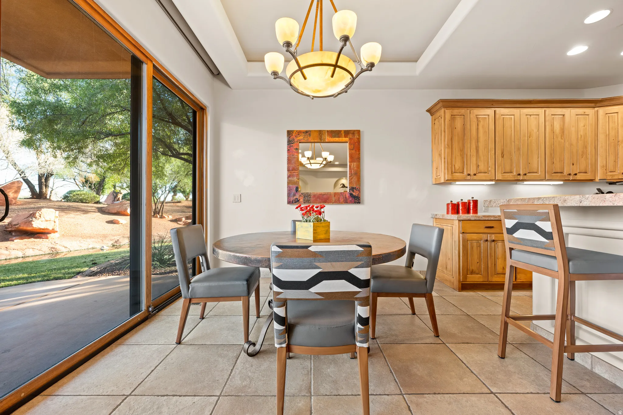 Recessed ceiling with a chandelier, wood-finish cabinetry, tile flooring, and a sliding glass door