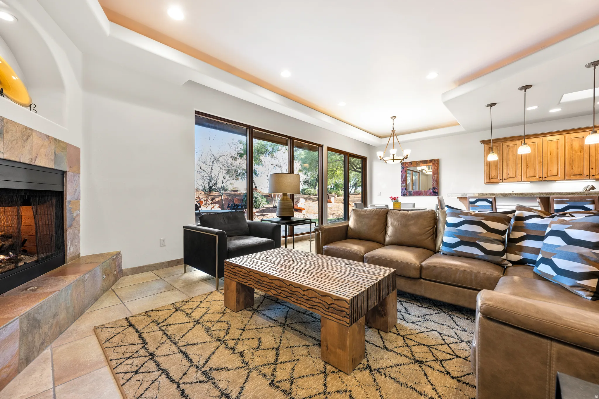 Tiled flooring throughout, large windows with exterior scenery, fireplace with stone surround, recessed lighting, and a tray ceiling