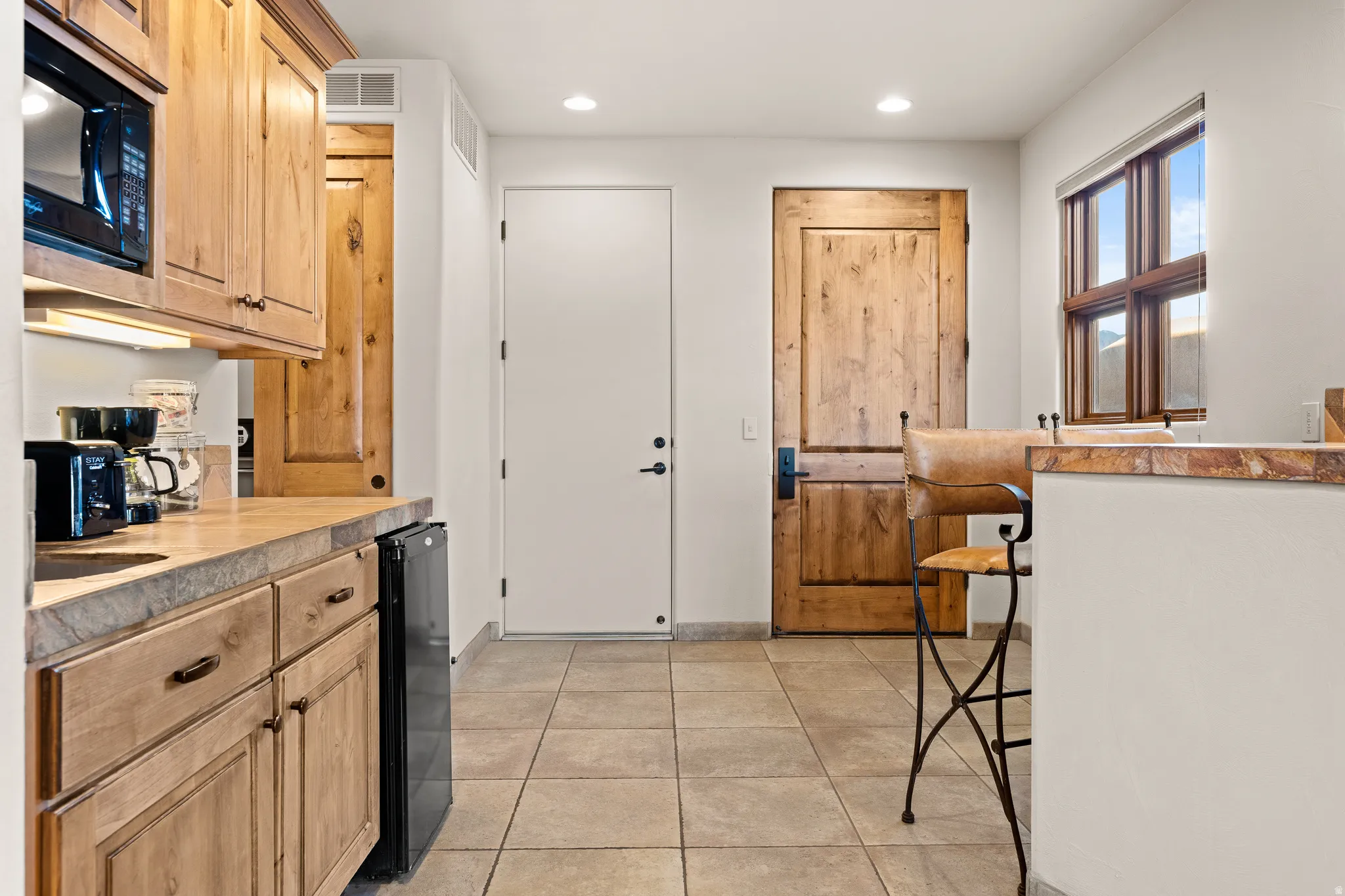 Wood cabinetry with a built-in microwave, tiled flooring, and a stone countertop