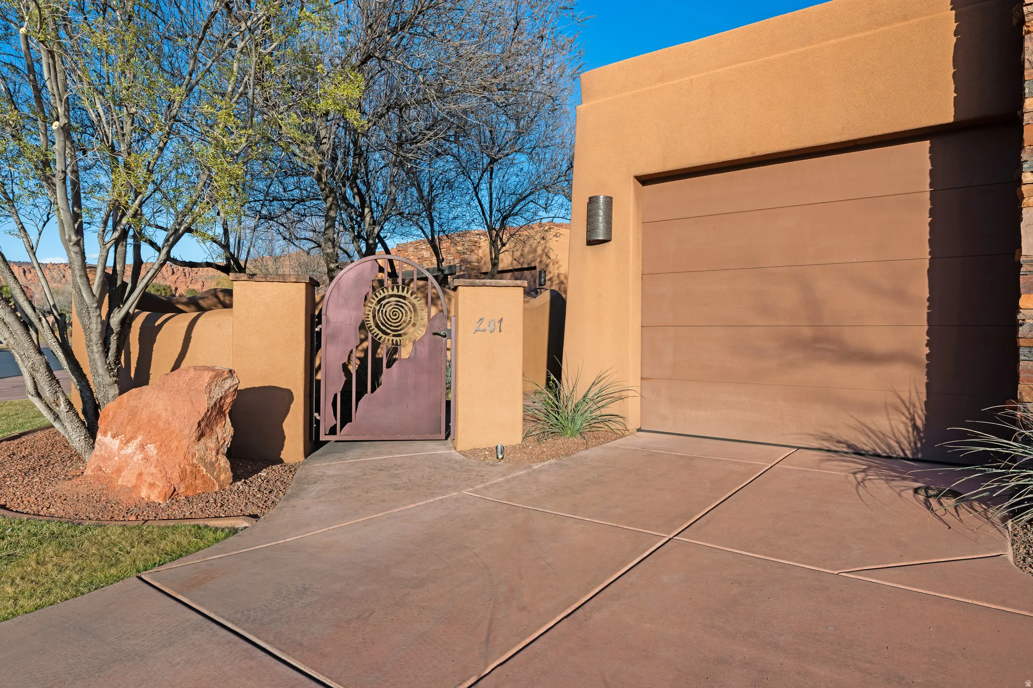 Stucco exterior with an integrated garage, decorative entry gate, concrete drive, and desert landscaping