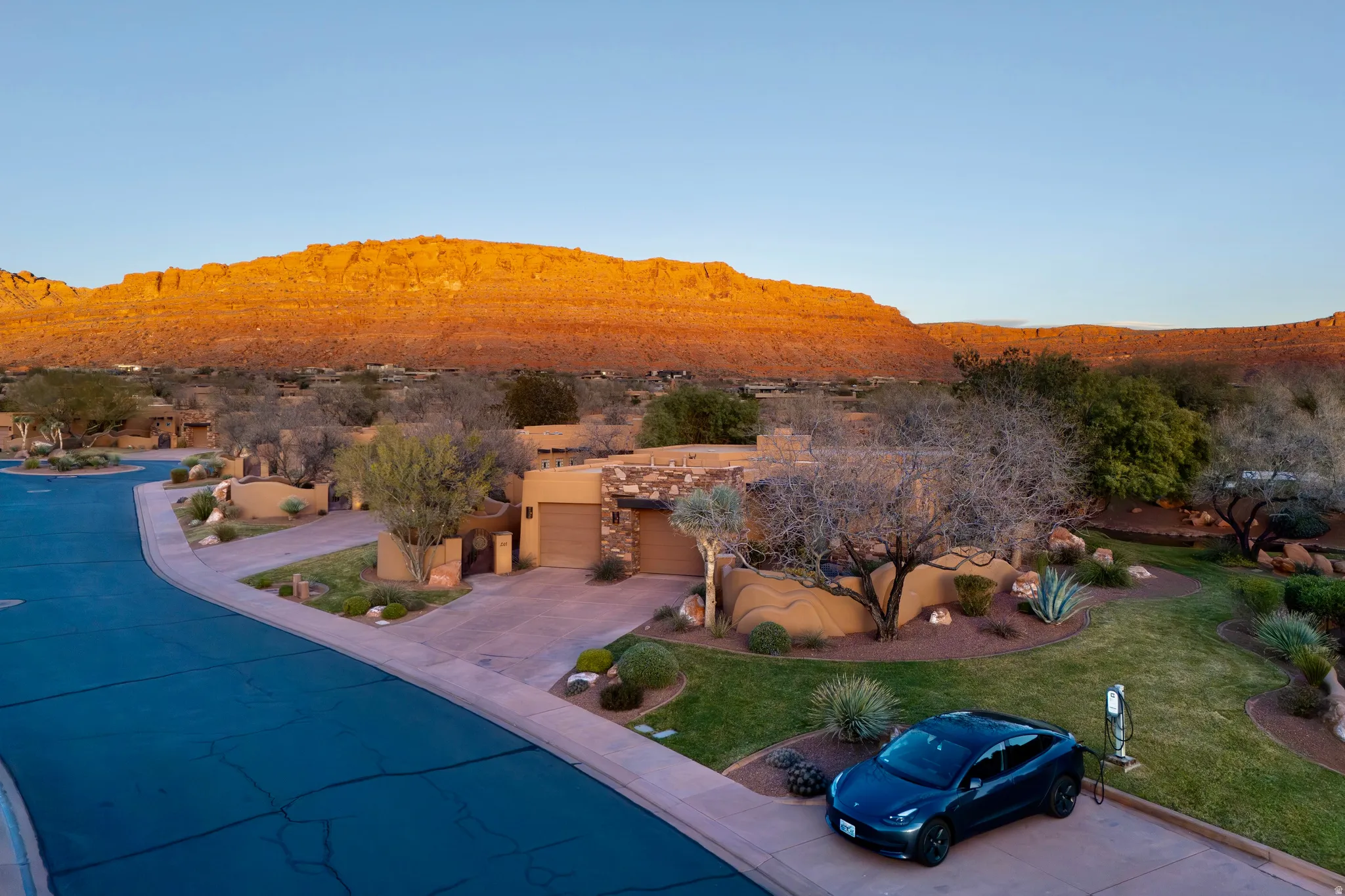 Stucco exterior with stone accents, attached garage, paved driveway, mature landscaping, and an exterior EV charging station