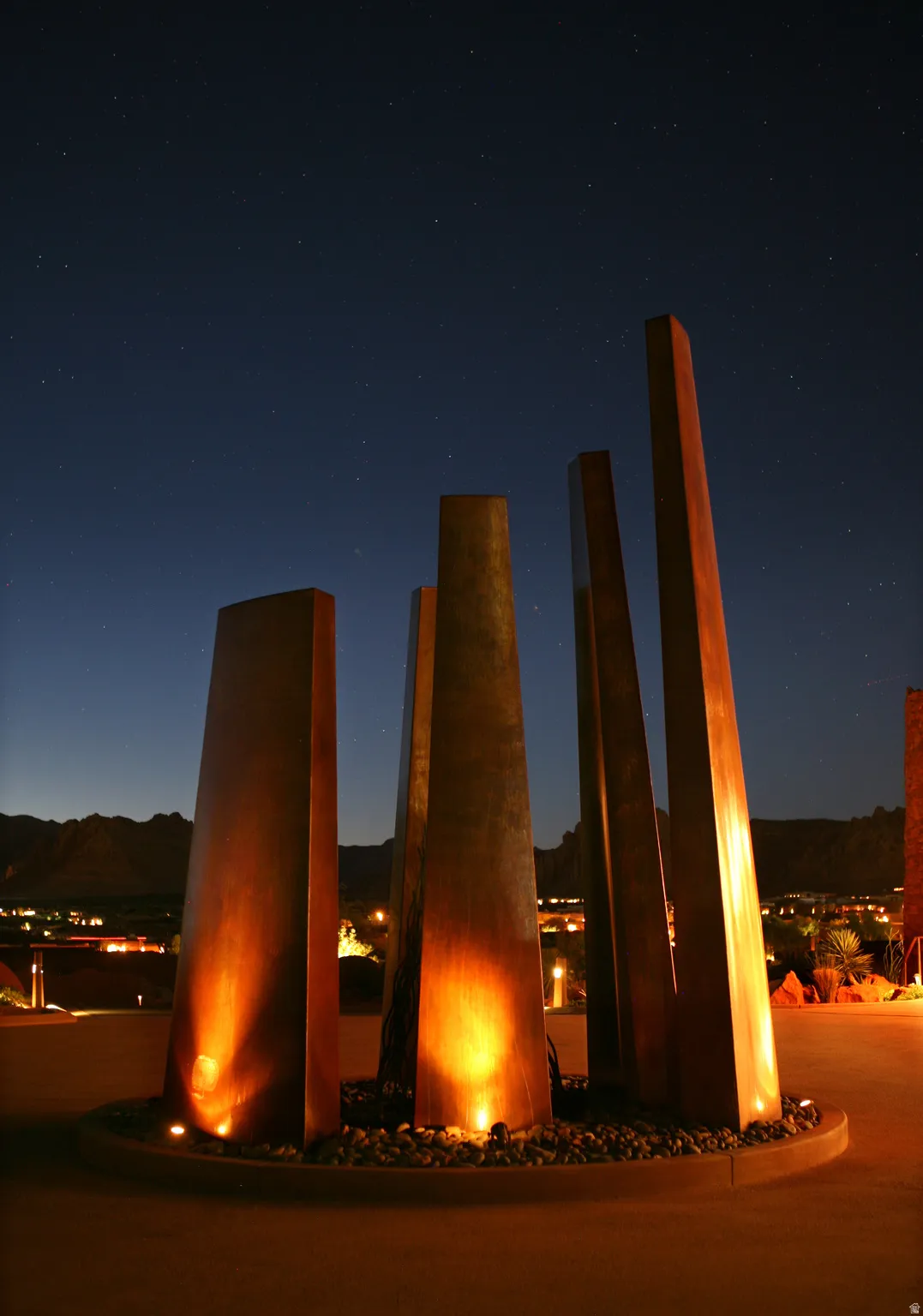 Architectural water feature with multiple upright panels, integrated accent lighting, and a dark aggregate base