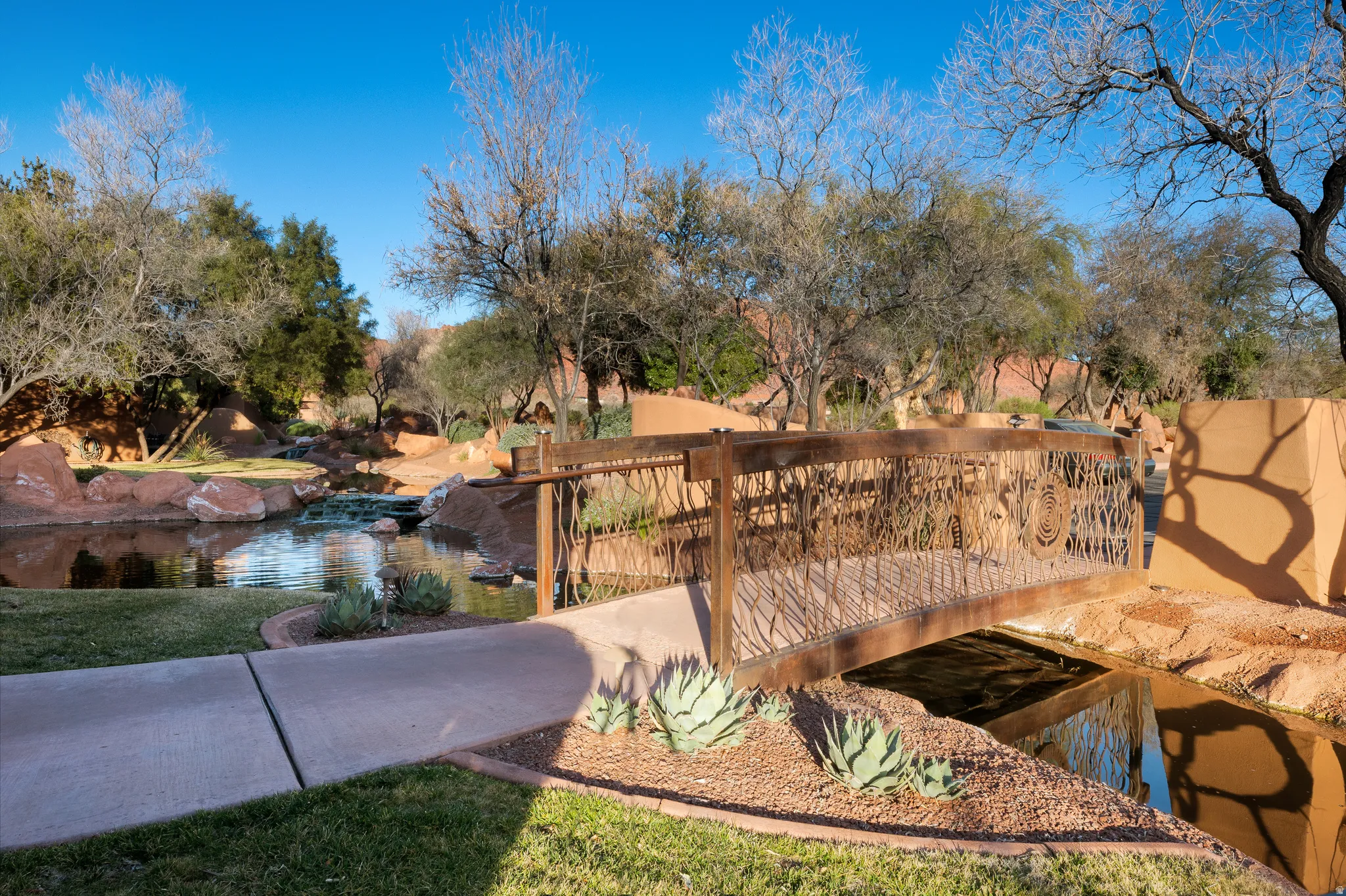Manicured landscaping with a decorative bridge, water feature, and a concrete pathway