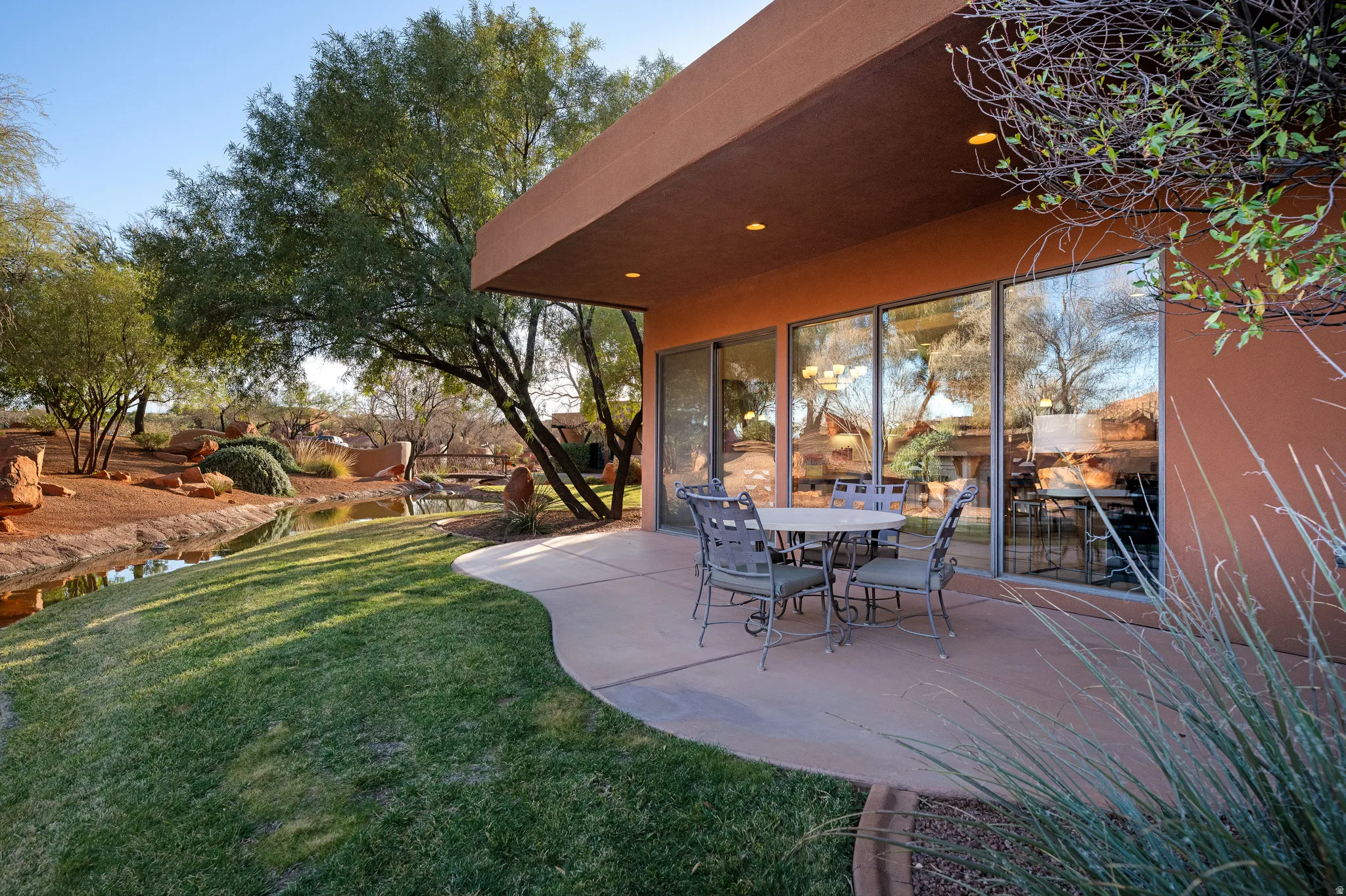 Curved patio with a stucco exterior, expansive glass sliding doors, recessed lighting, and a landscaped yard with a water feature