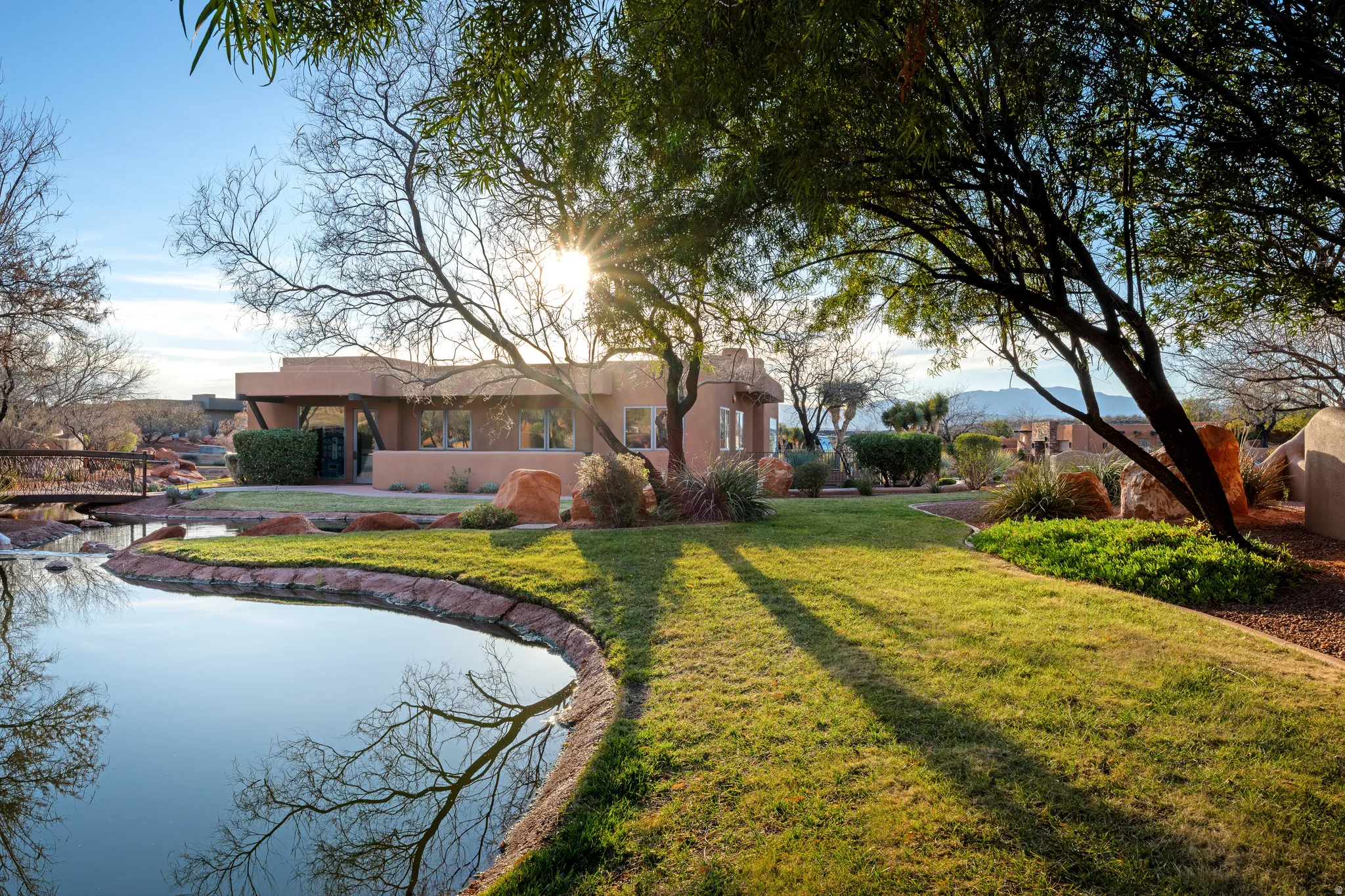 Expansive lawn area with a reflective water feature, mature trees, and a wooden bridge